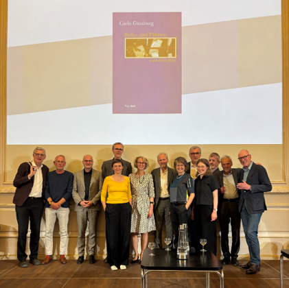 Gruppenfoto: Autor:innen des Wagenbach-Verlags mit der Verlegerin, auf der Leinwand im Hintergrund ist ein Buchcover von Carlo Ginzburg zu sehen